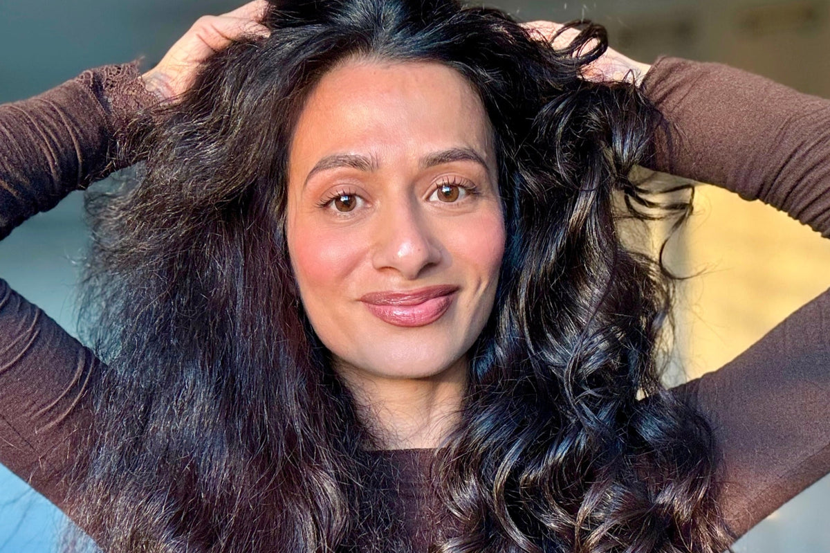 Portrait de Laial Darwich, fondatrice AIA Curls, mains dans ses cheveux bouclés naturels